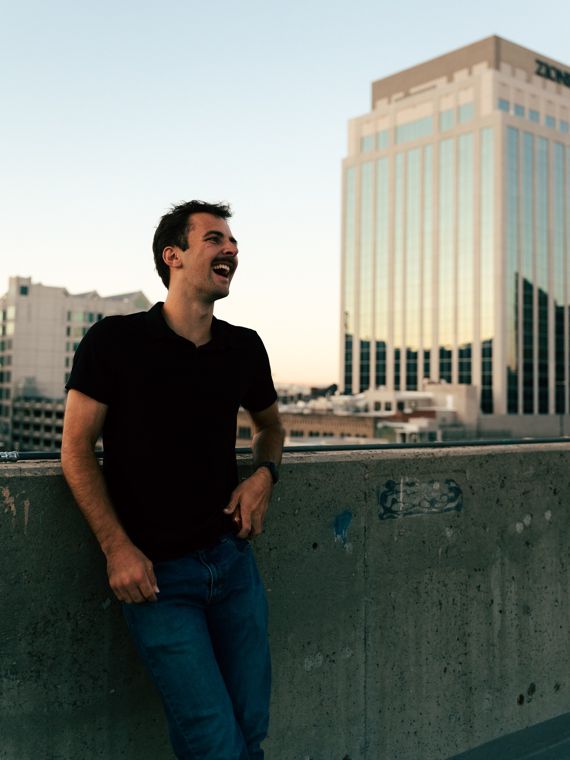 Trace Keller laughing on a rooftop wall with downtown Boise behind him