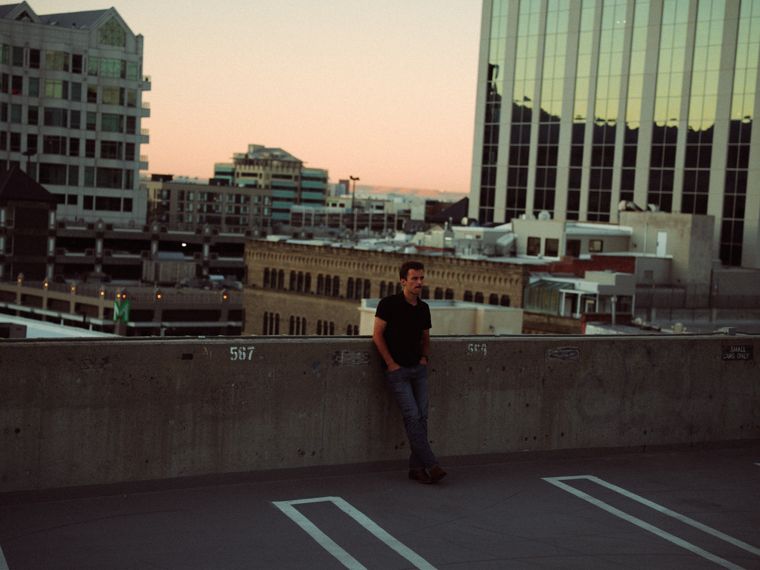 Trace Keller leaning on a rooftop wall at dusk, small in the frame