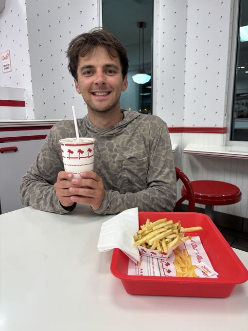 Smiling man holding a milkshake with fries at In-N-Out
