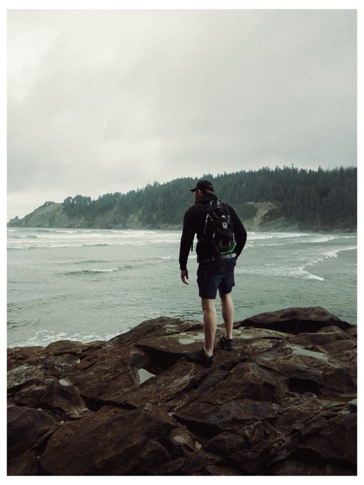 Hiker with a backpack standing on rocks looking out at ocean waves