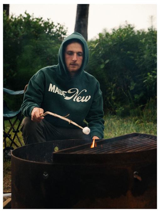 Man in a Made New hoodie roasting a marshmallow over a campfire