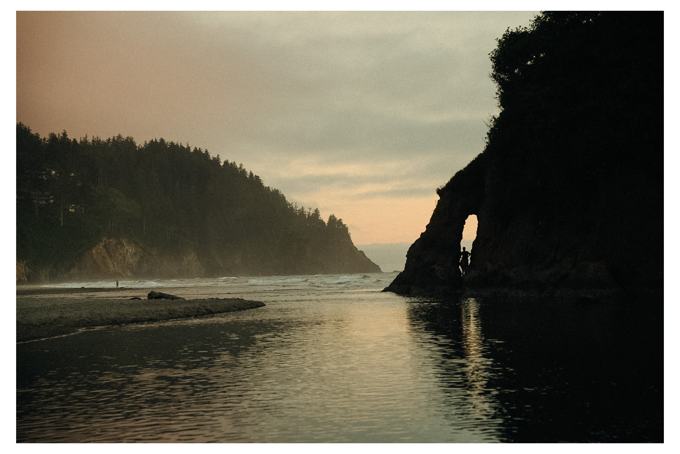 Silhouette of a person standing in a sea arch at sunset over a tidal inlet