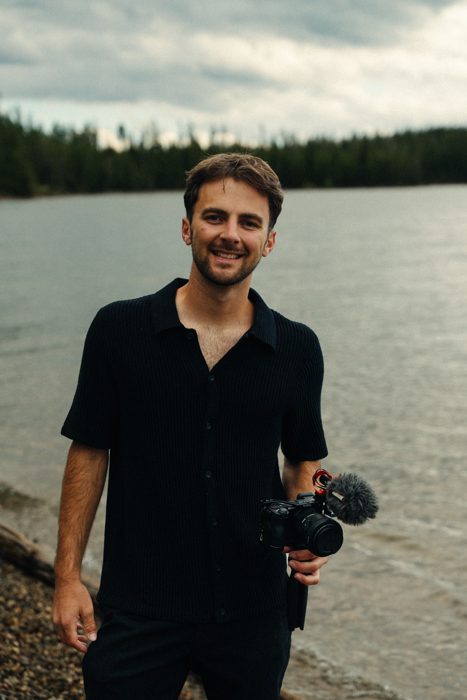 Trace Keller, Boise wedding photographer and videographer, holding a video camera by a lake