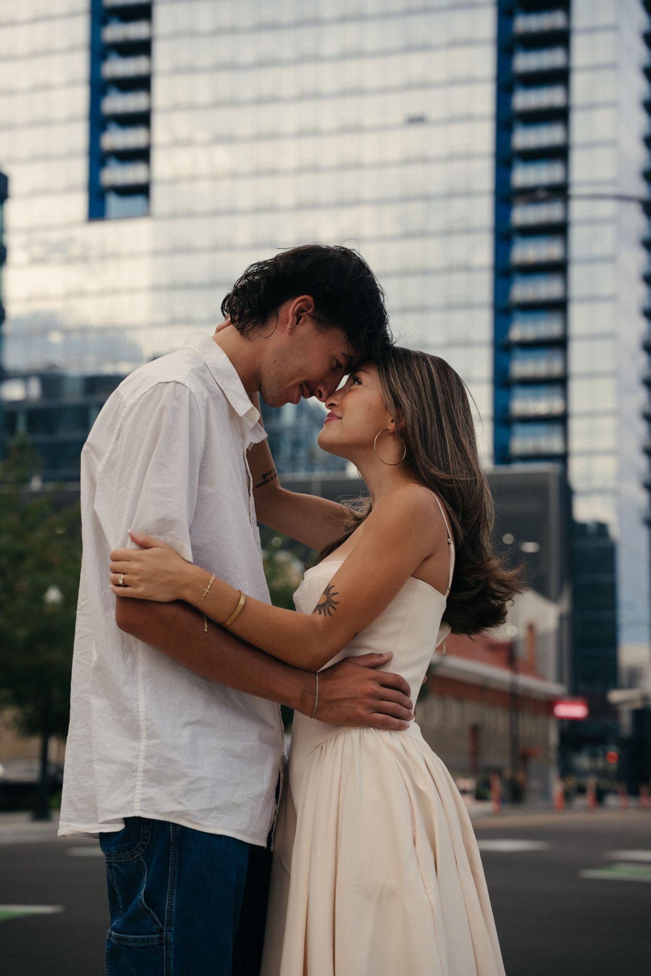 Lucas and Audry touching foreheads and smiling on a downtown street in front of a glass tower