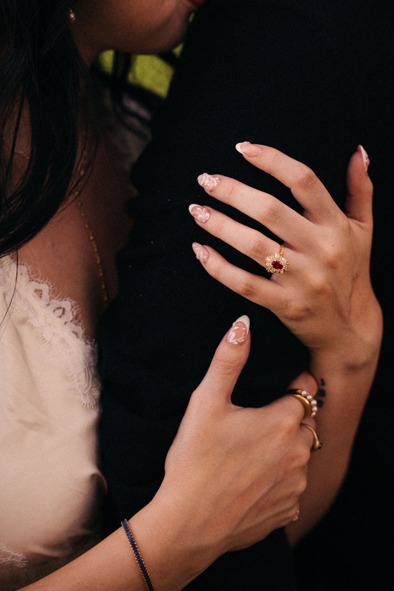 Close-up of Cora's hands with floral nail art and a ruby and diamond ring resting on James's black sweater