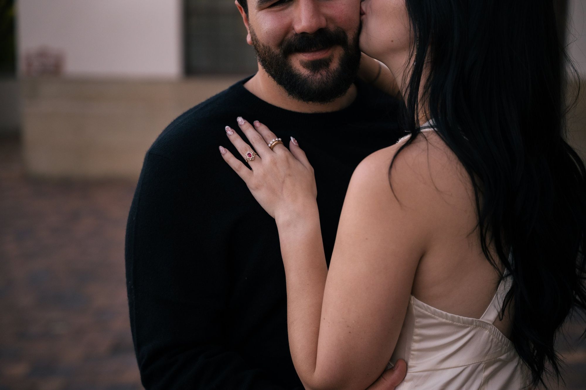 Cora kisses James on the cheek as he smiles, her ruby ring resting on his black sweater