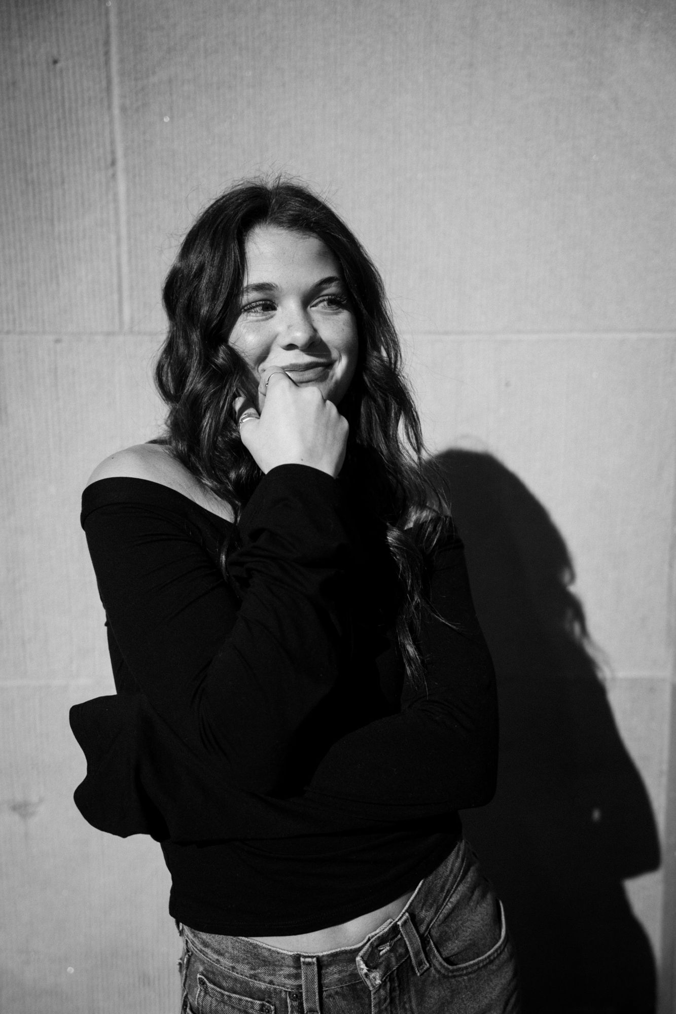 Adeline smiling and looking off to the side with her hand at her chin, in black and white, her shadow on the wall behind her