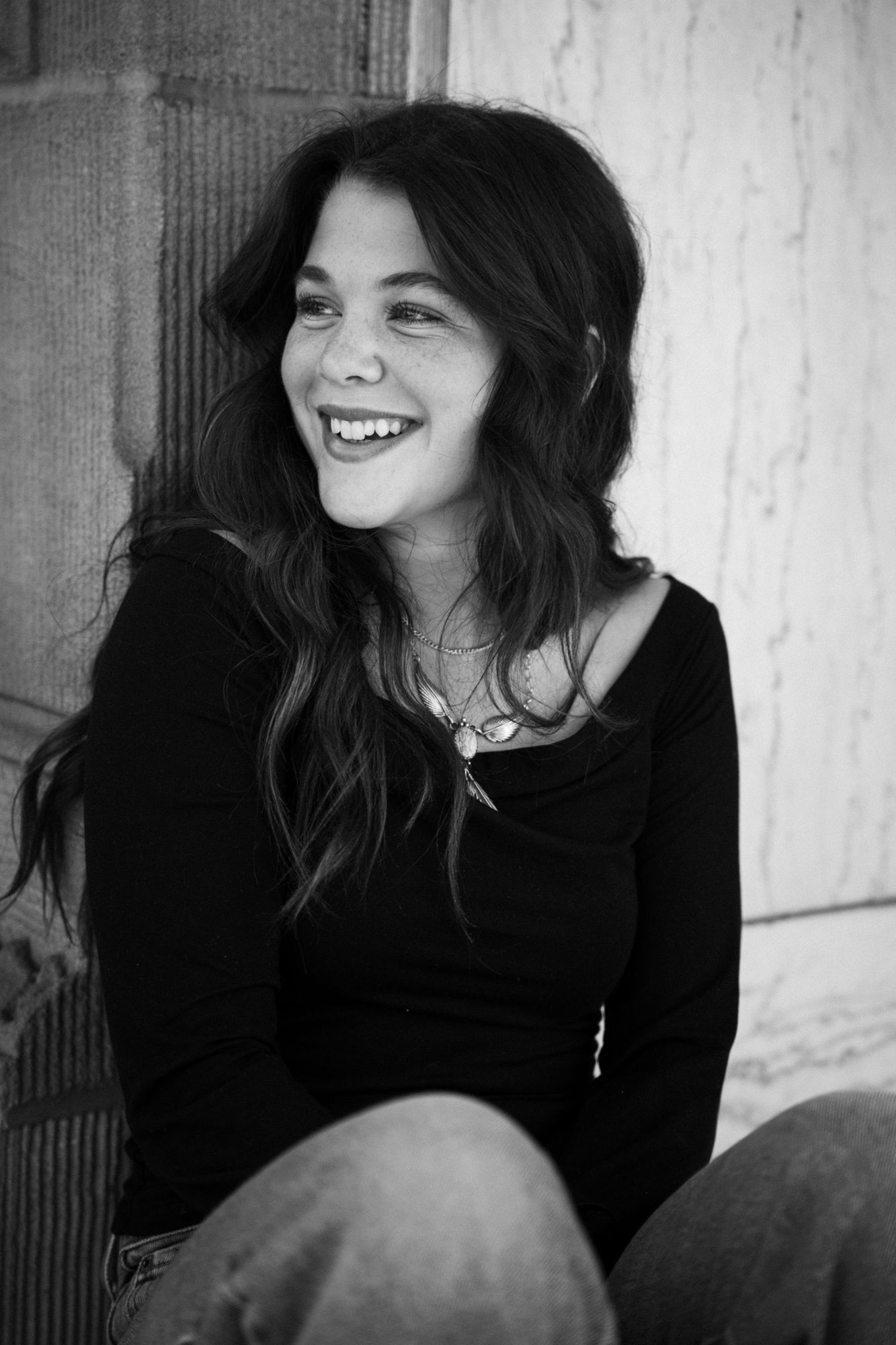 Adeline laughing and looking off to the side in black and white, seated in front of a stone and marble wall