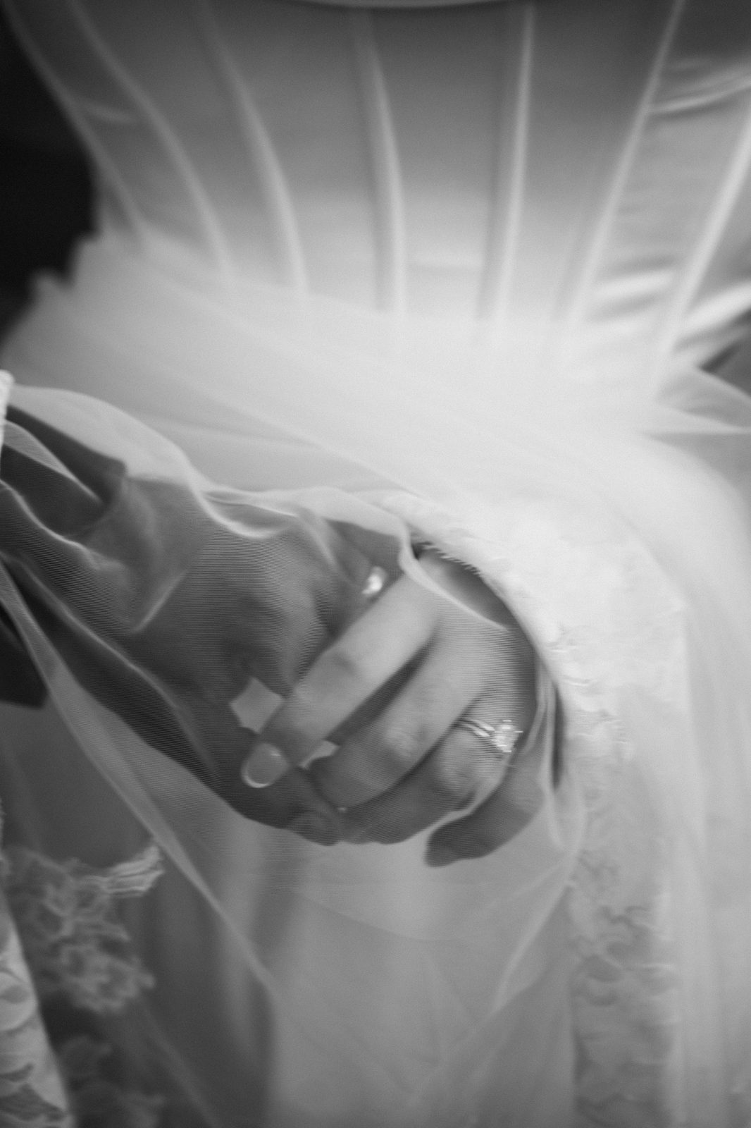 Black and white detail of Trinity's hand with her rings resting on Caio's hand, framed by her veil and wedding dress