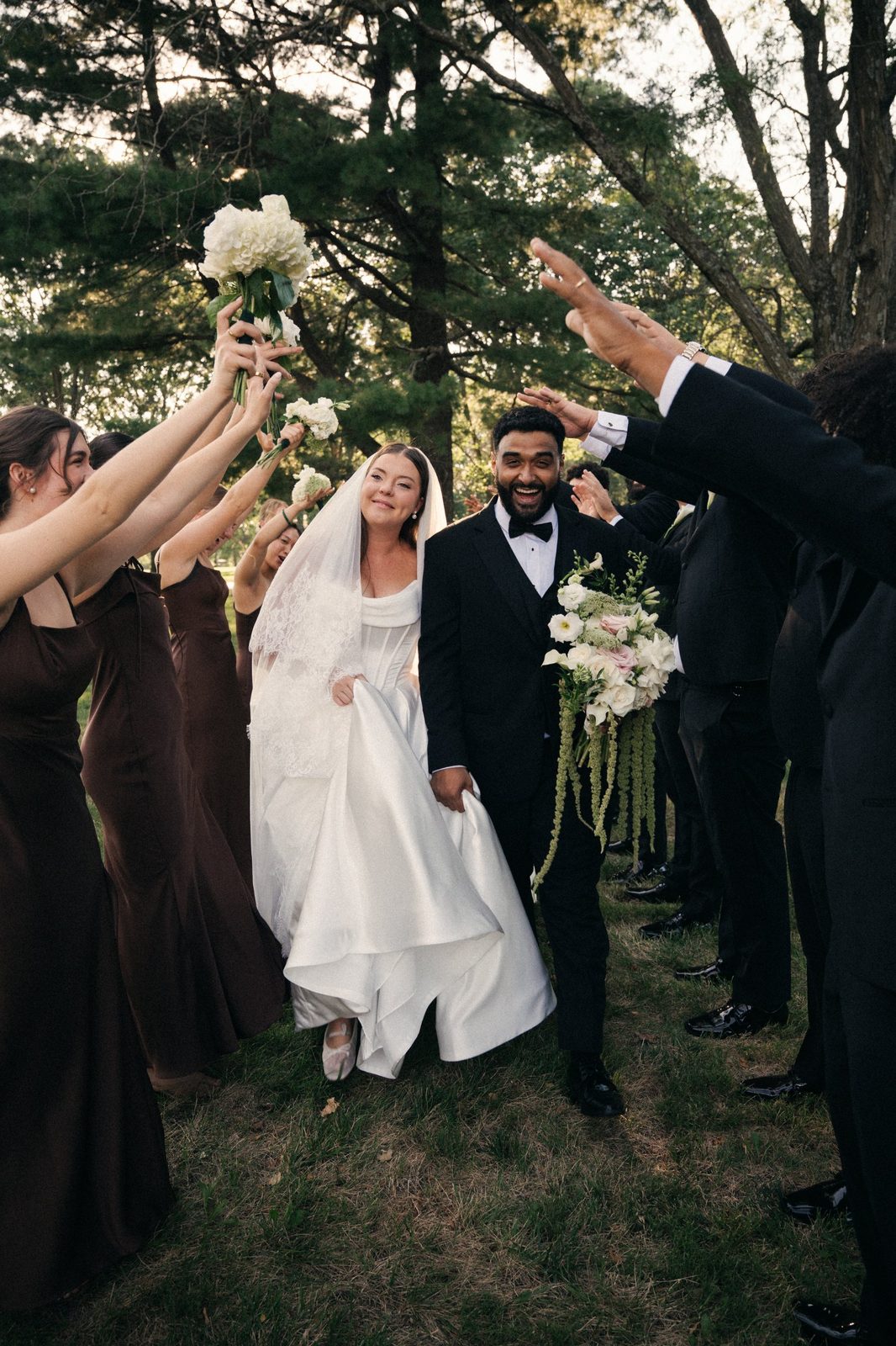 Caio and Trinity walking through an arch of raised hands and bouquets formed by their wedding party