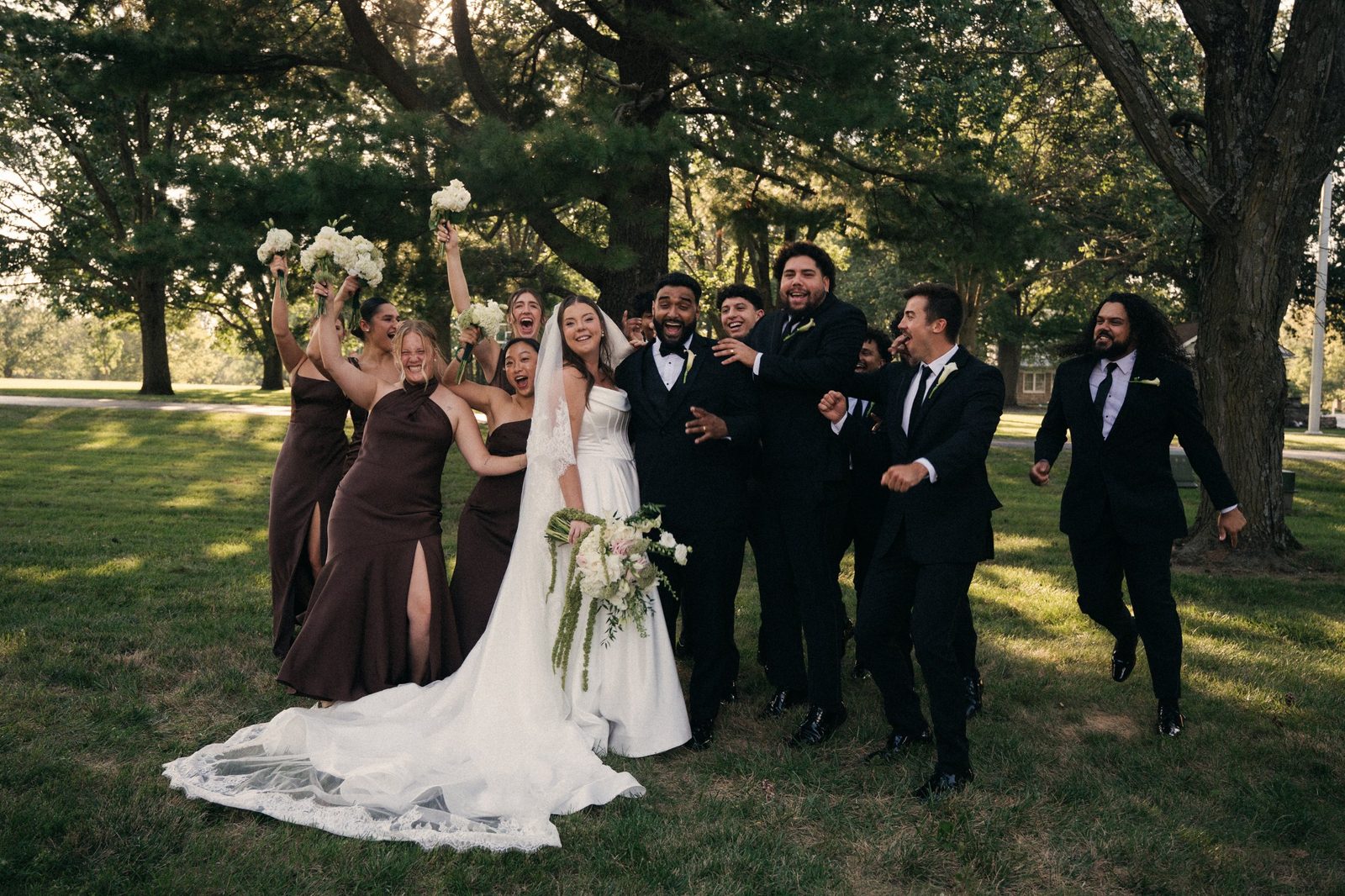 Caio and Trinity laughing with their bridesmaids in brown dresses and groomsmen in black as the wedding party cheers around them