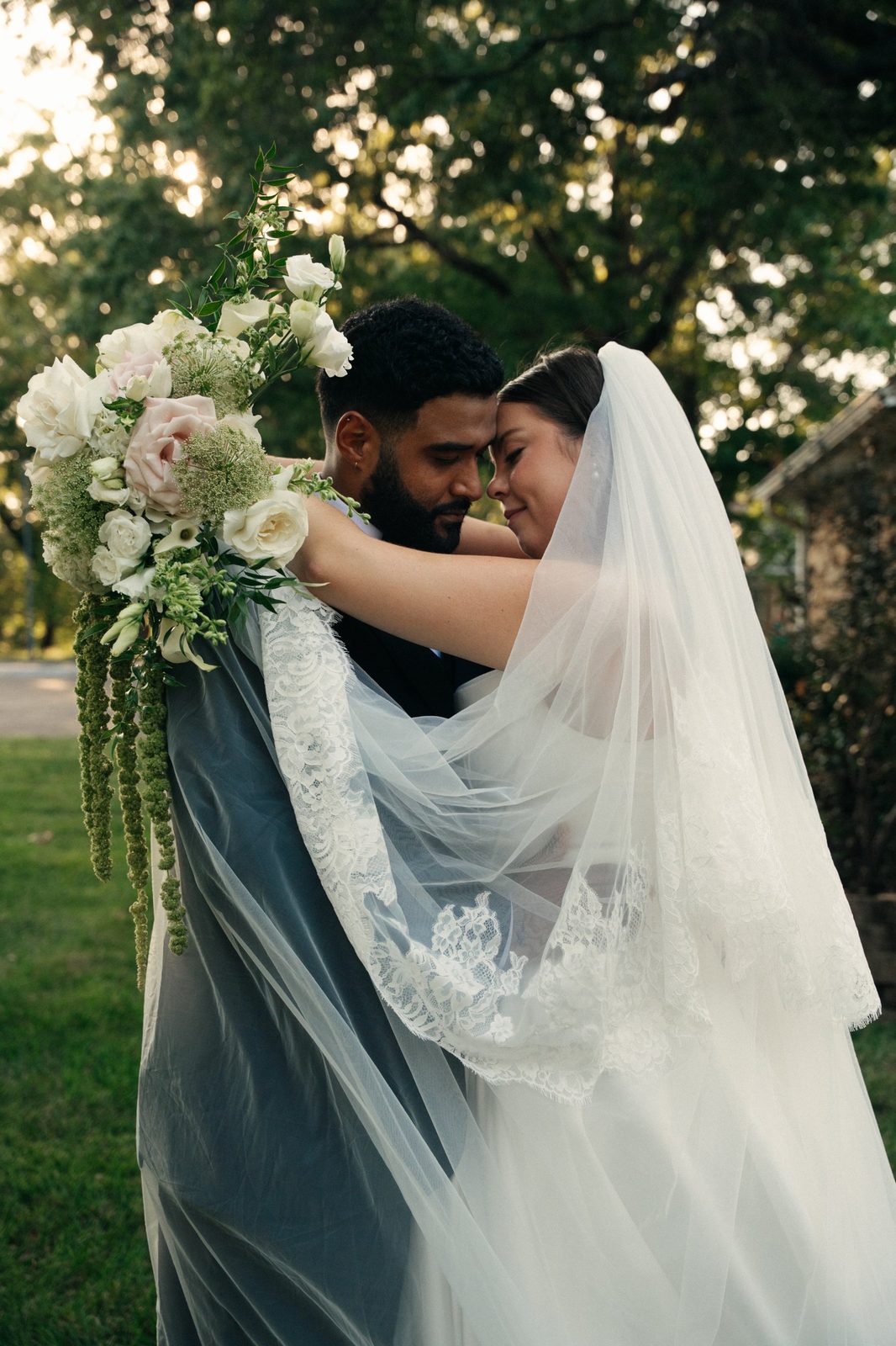 Caio and Trinity embracing with her veil and a hanging bouquet wrapped around them