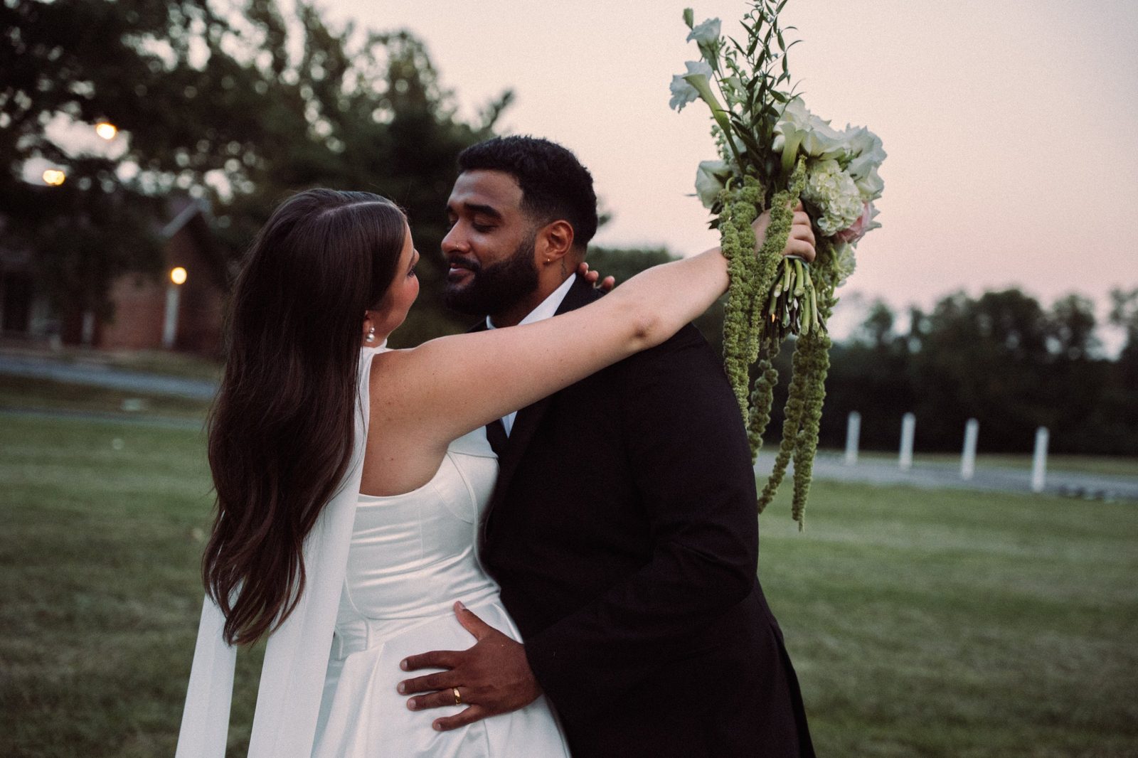 Trinity holding her bouquet high as she and Caio share a close moment in the pink light after sunset