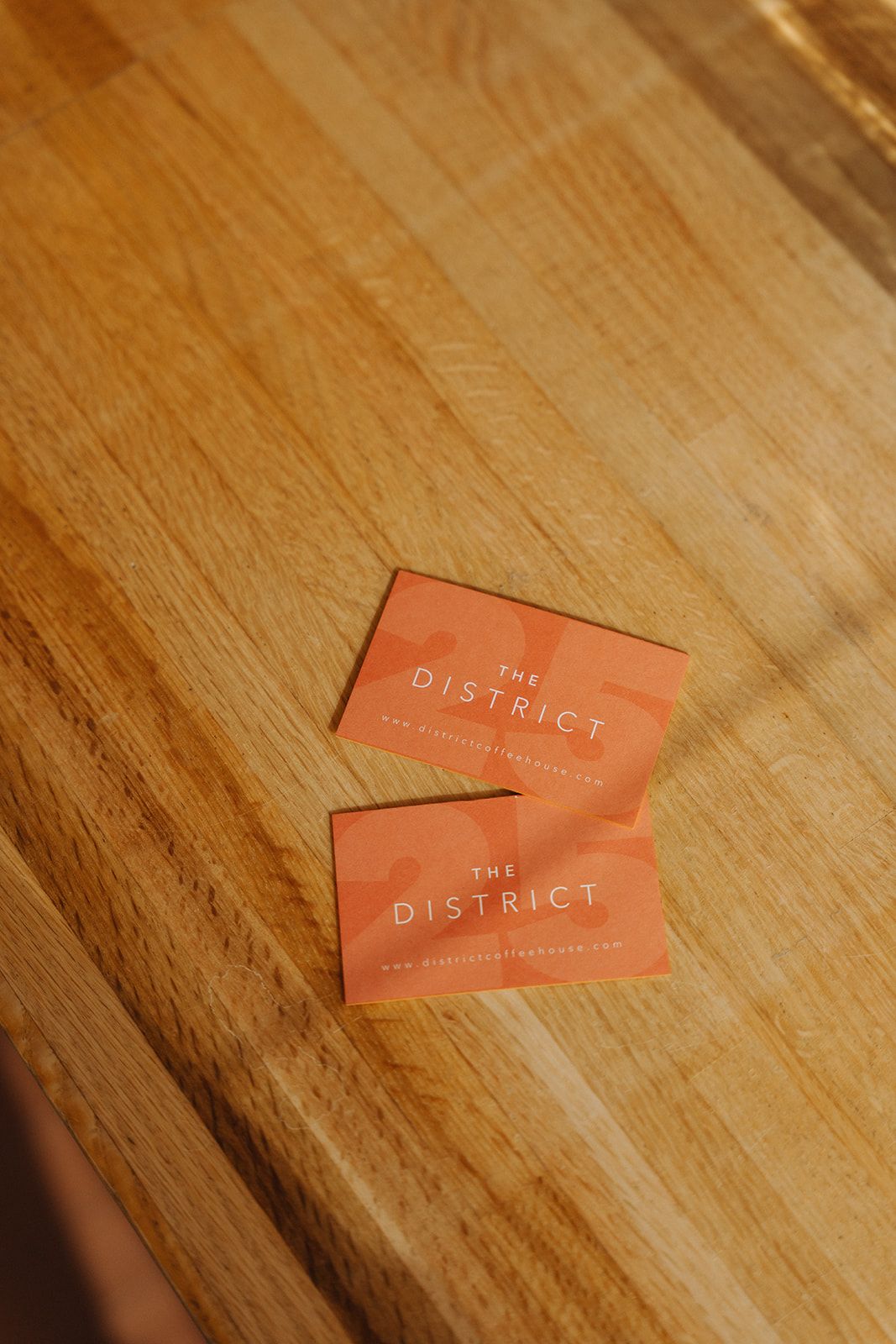 Two orange District Coffee House cards resting on a warm wooden countertop