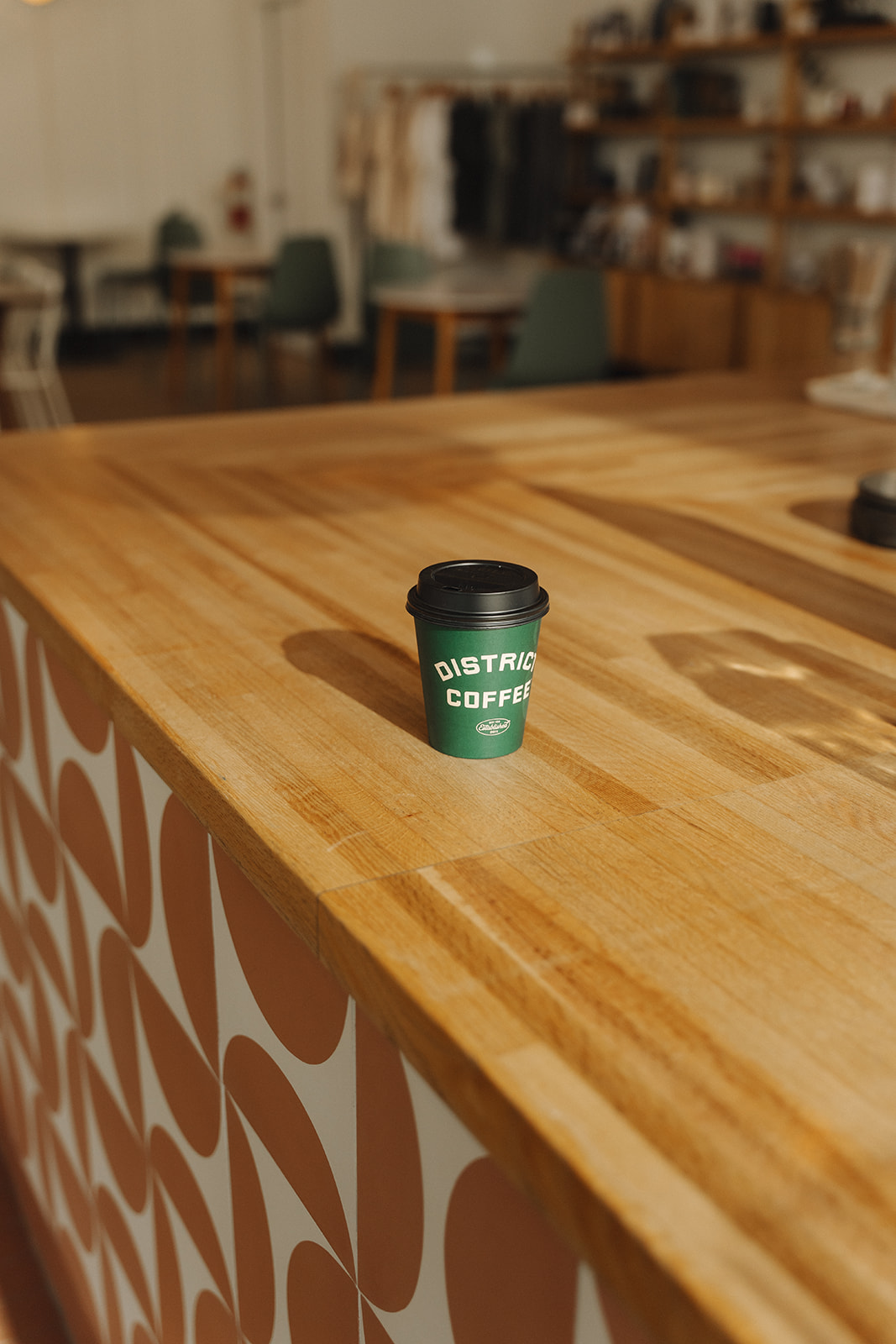 Green District Coffee takeaway cup on the butcher block counter in warm morning light