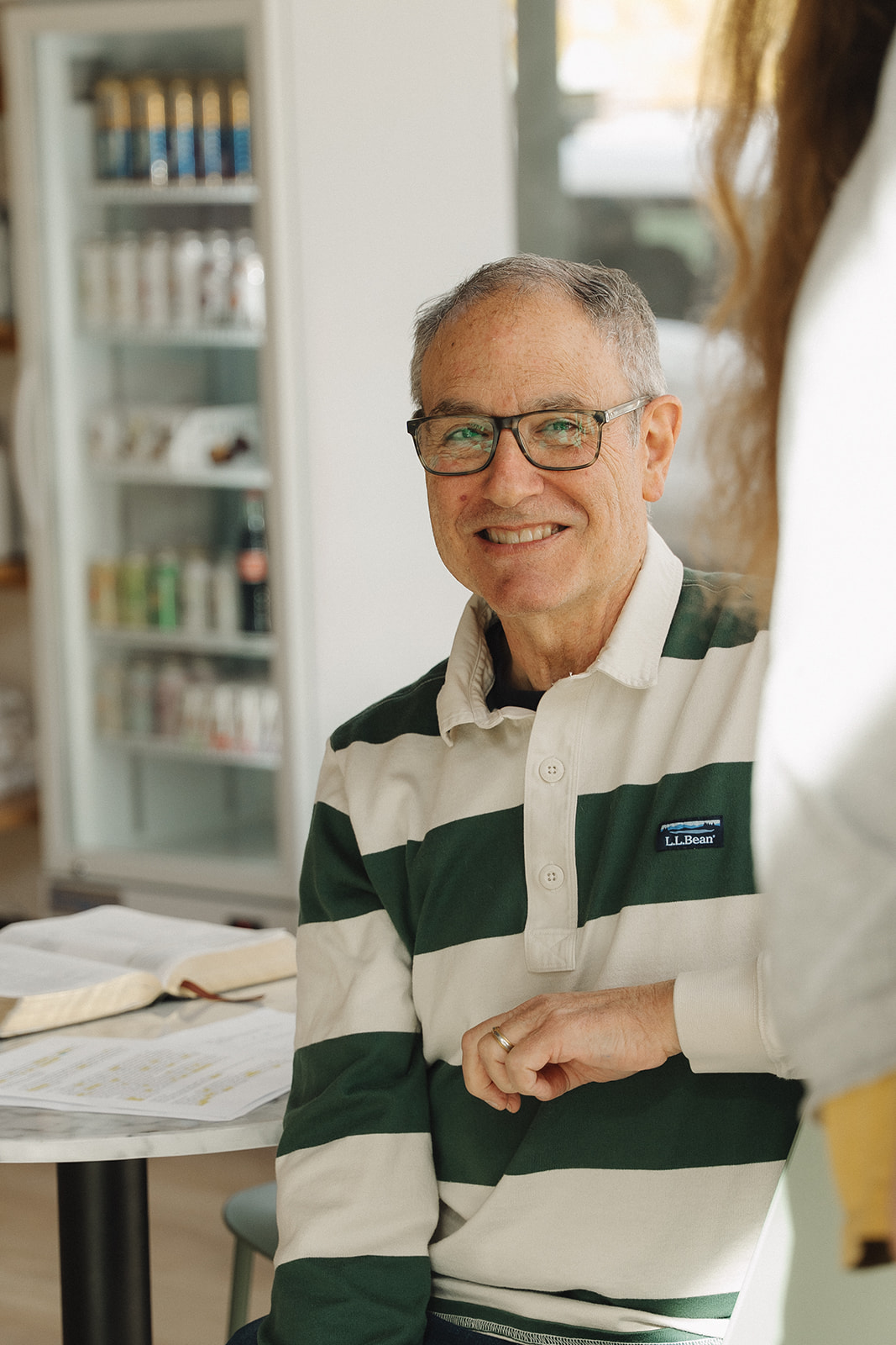 Man in glasses and a green striped rugby shirt smiling at a table with an open book and papers