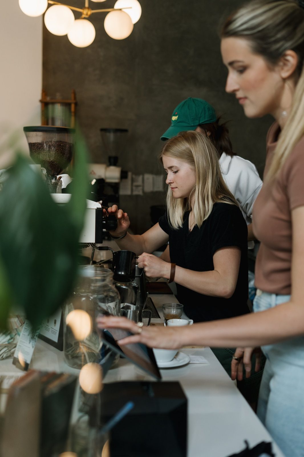 Two baristas making drinks at the espresso machine while a customer taps a screen in the foreground