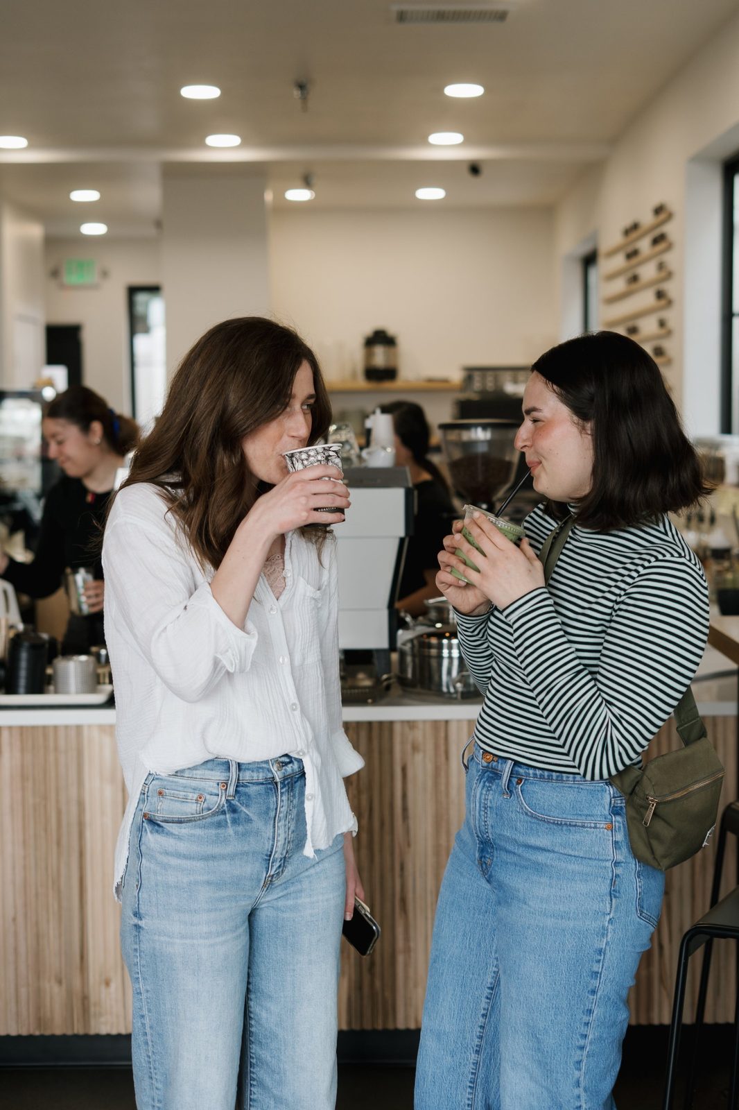 Two friends laughing while drinking a coffee and a matcha at the counter