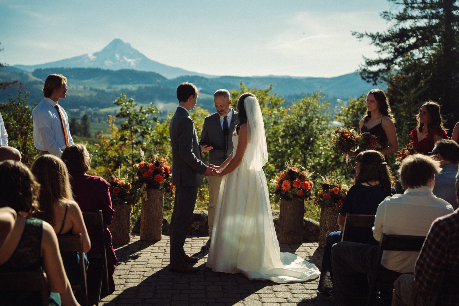 Madeline and Jonathan hold hands during their outdoor ceremony in Hood River, Oregon, with Mount Hood and autumn flowers behind them