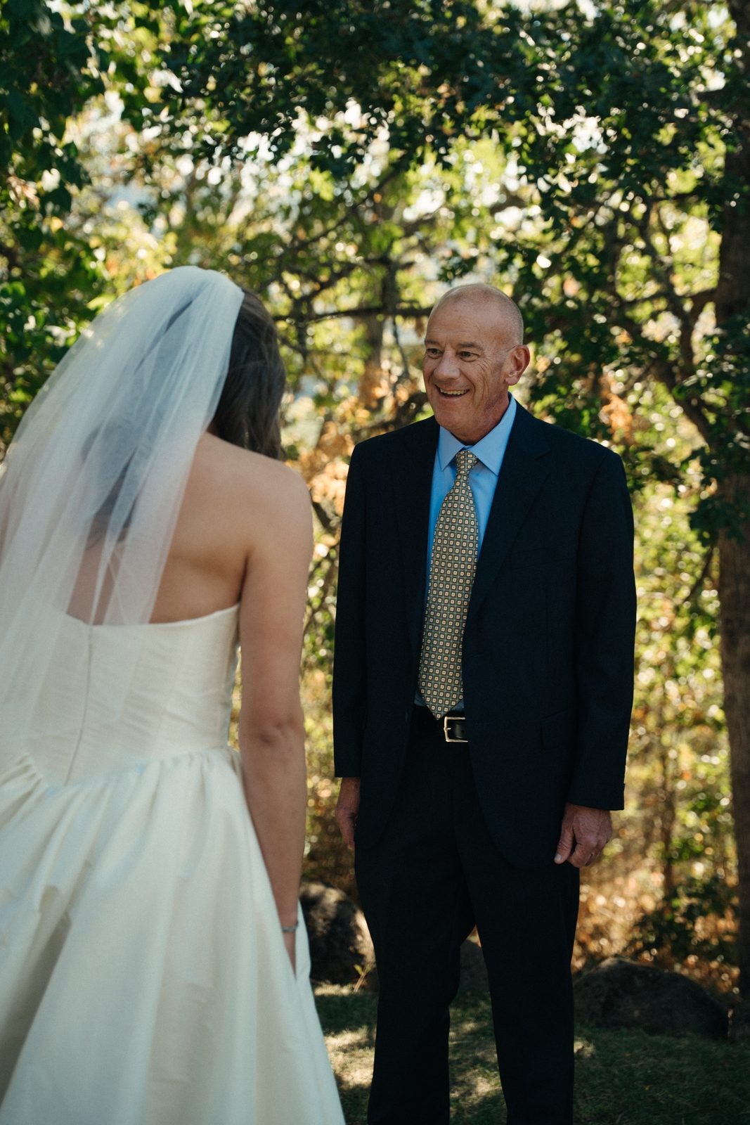 Bride's father smiling with joy during their first look under the trees