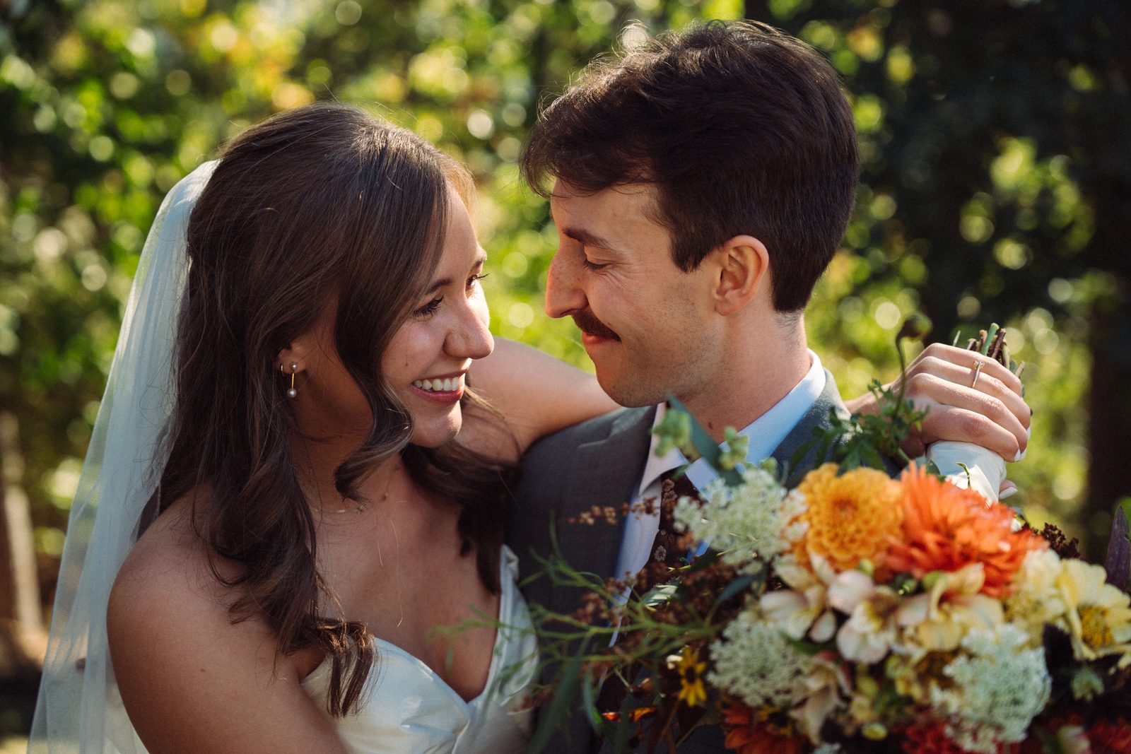 Bride and groom gazing at each other, an orange and cream dahlia bouquet in front