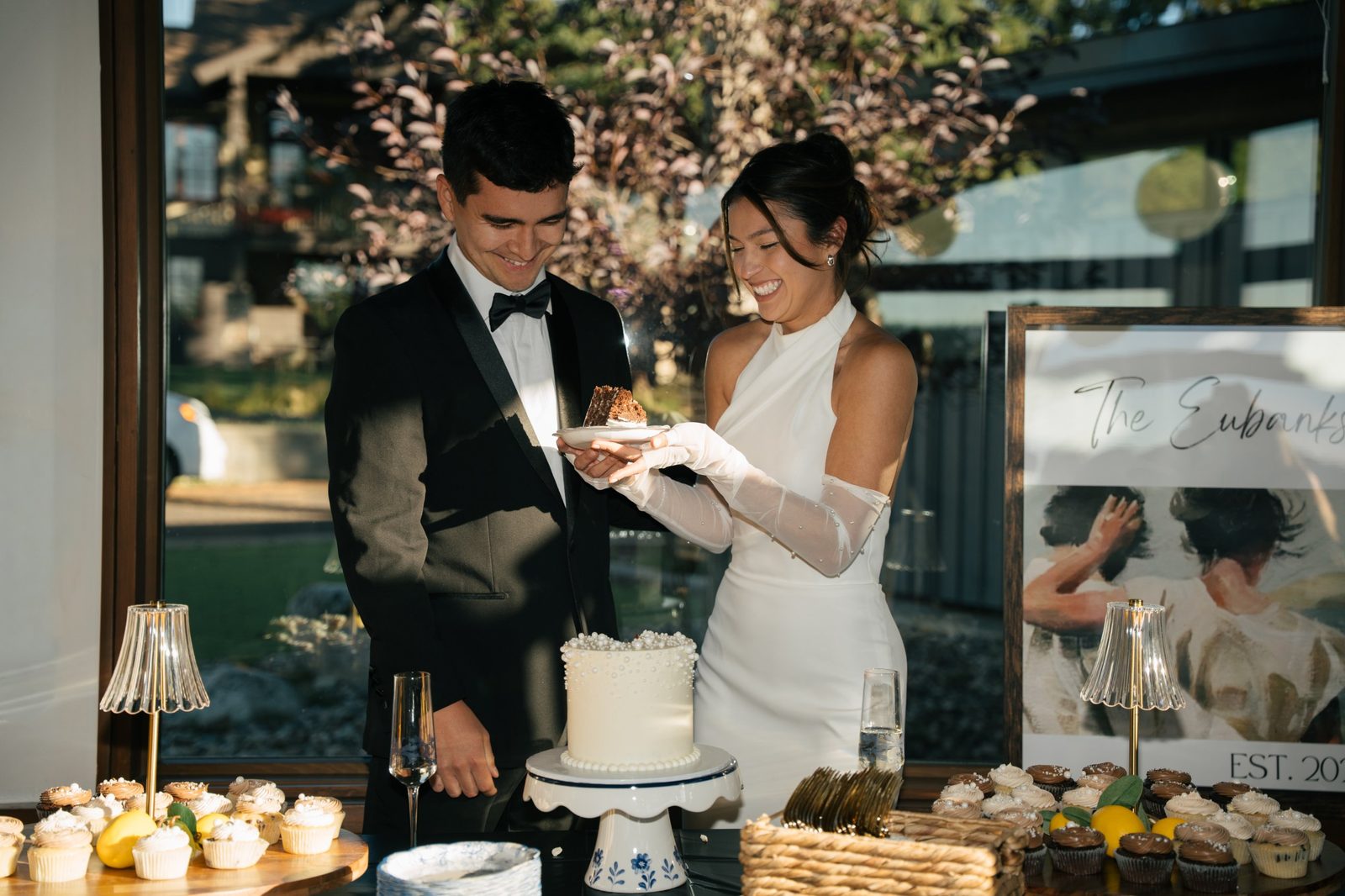 Skyler and Becca laughing as they cut a pearl-covered cake surrounded by lemon cupcakes