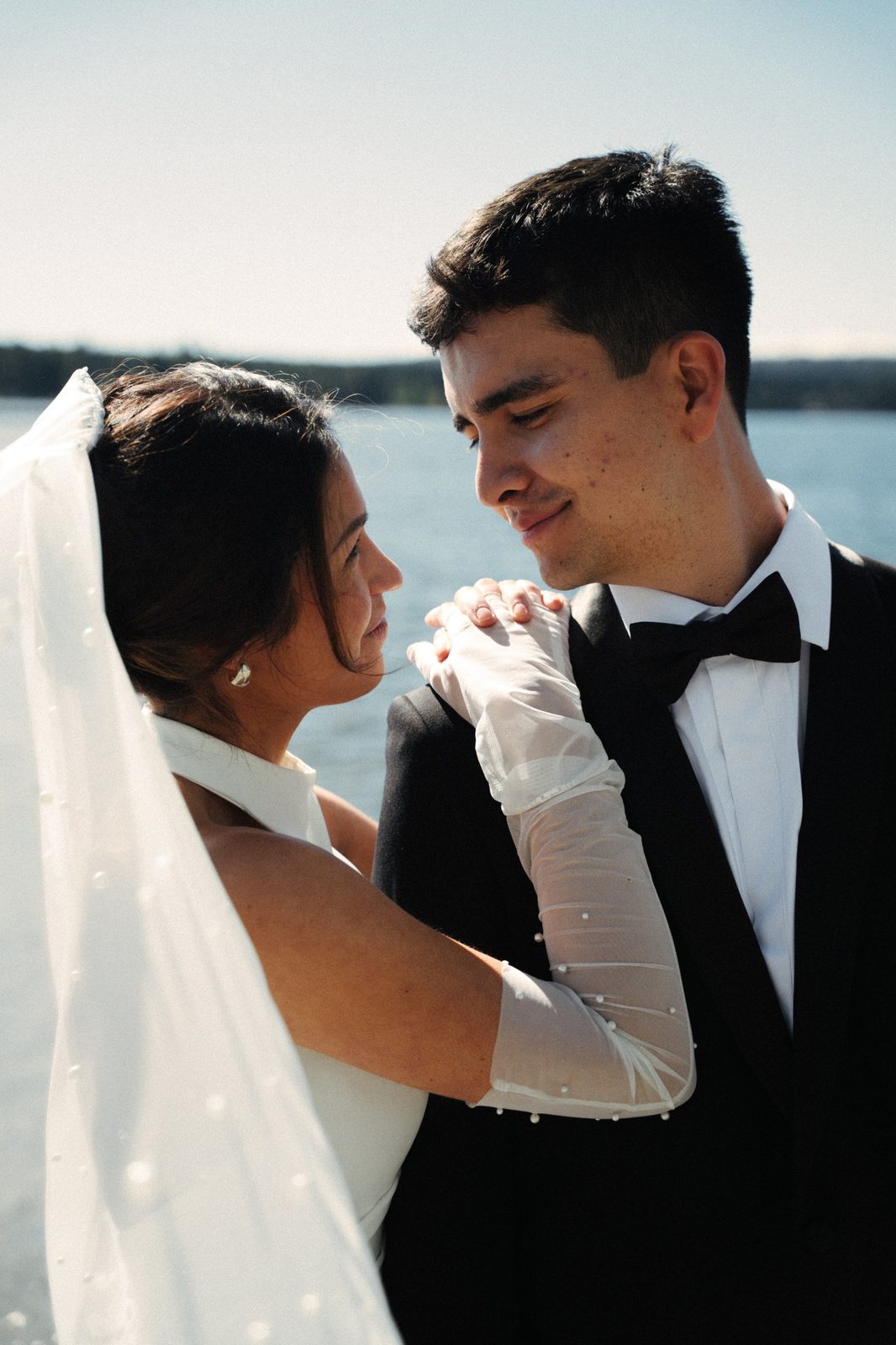 Skyler and Becca gazing at each other with the lake behind them, her pearl veil blowing across the frame