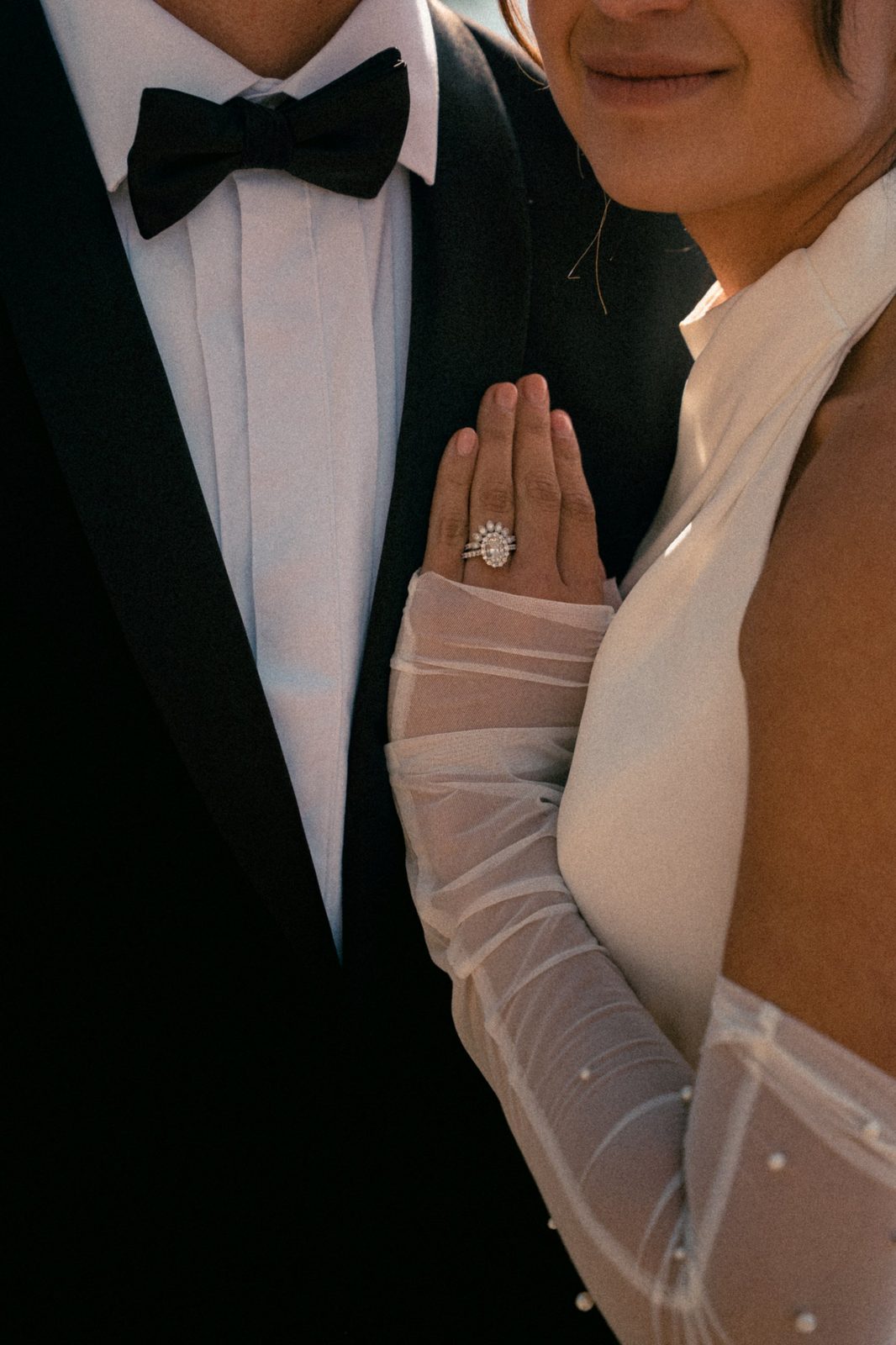 Close-up of Becca’s engagement ring and wedding band as her hand rests on Skyler’s tuxedo lapel