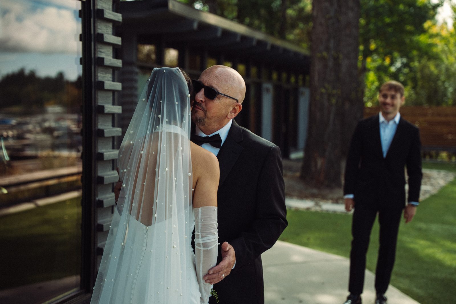 Becca hugging her dad during their first look while Skyler watches and smiles from the lawn
