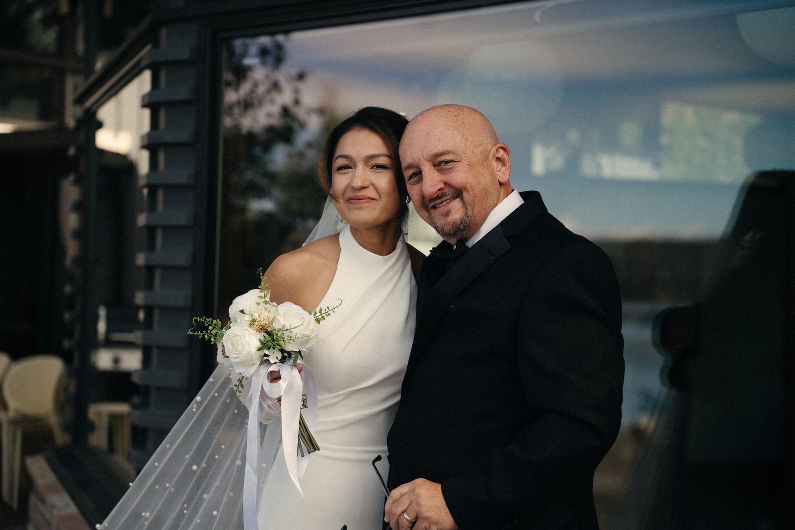 Becca and her dad cheek to cheek and smiling, with a lake reflected in the window behind them