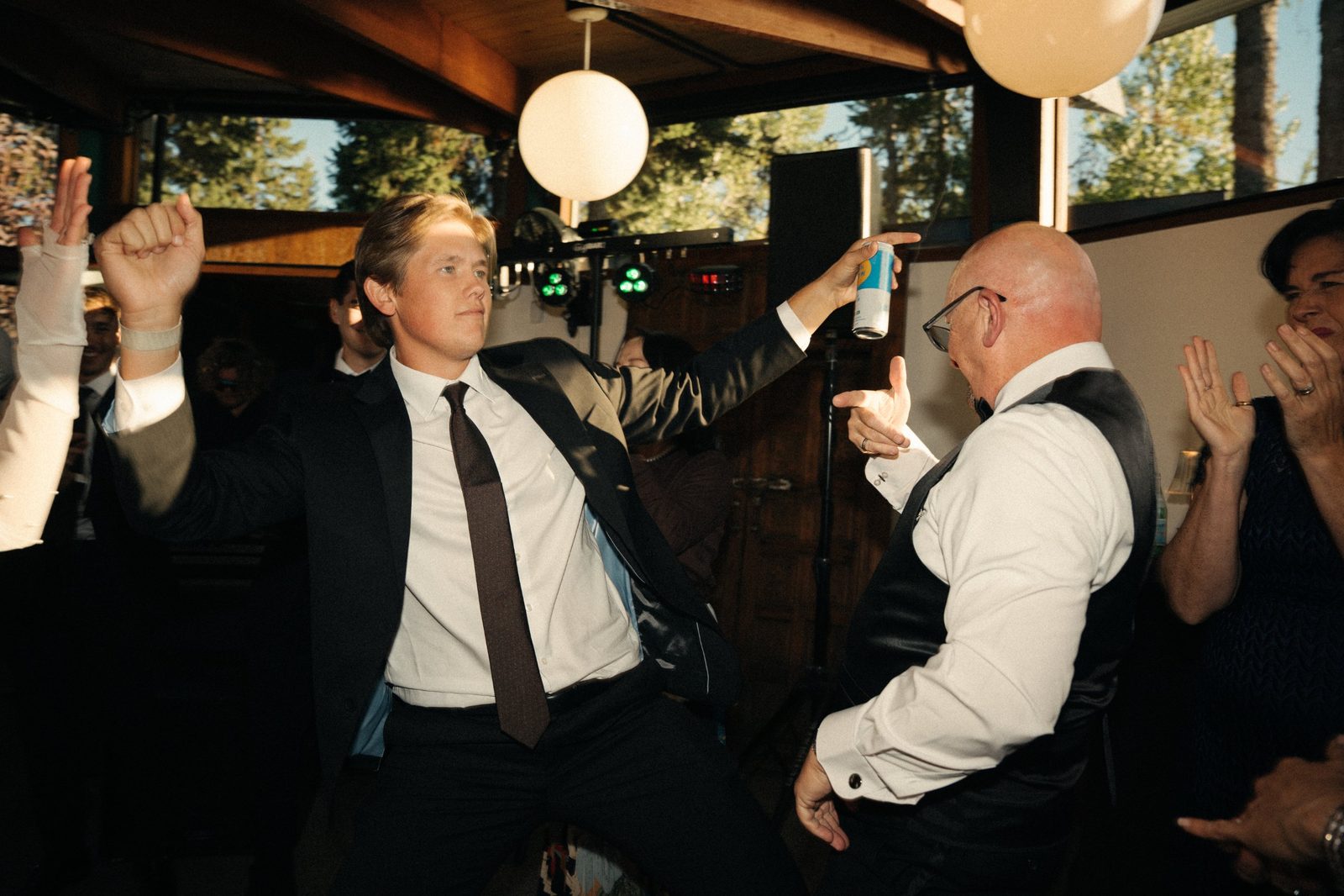 A groomsman and Becca’s dad dancing and pointing at each other on the dance floor as guests clap