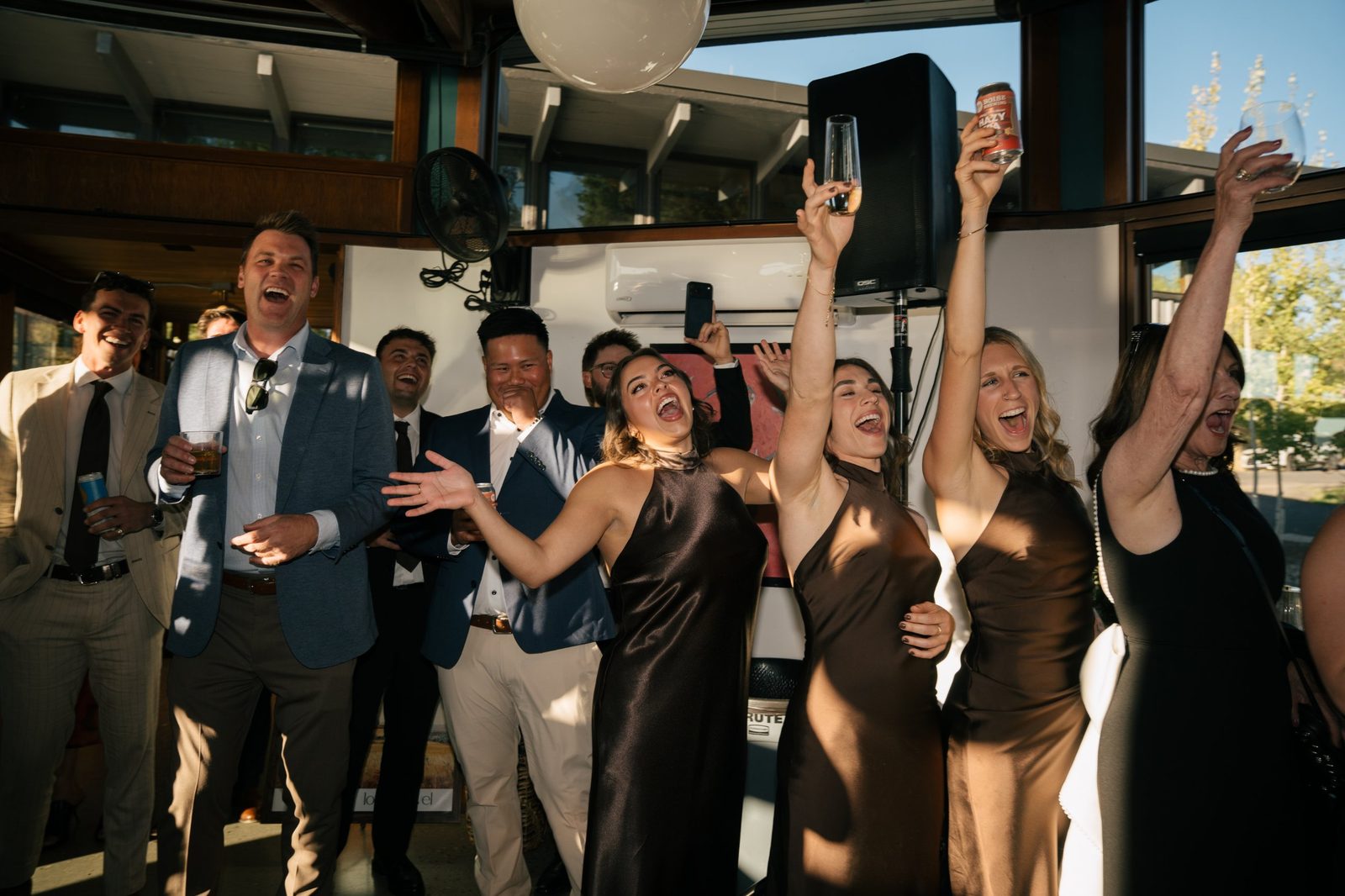 Wedding guests and bridesmaids cheering with drinks raised high at the reception