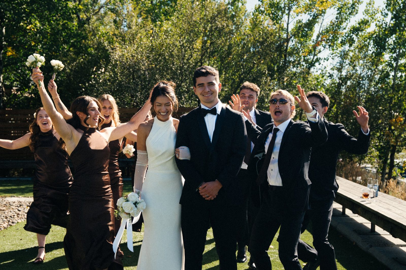 Becca and Skyler walking arm in arm while the bridesmaids and groomsmen cheer and wave behind them