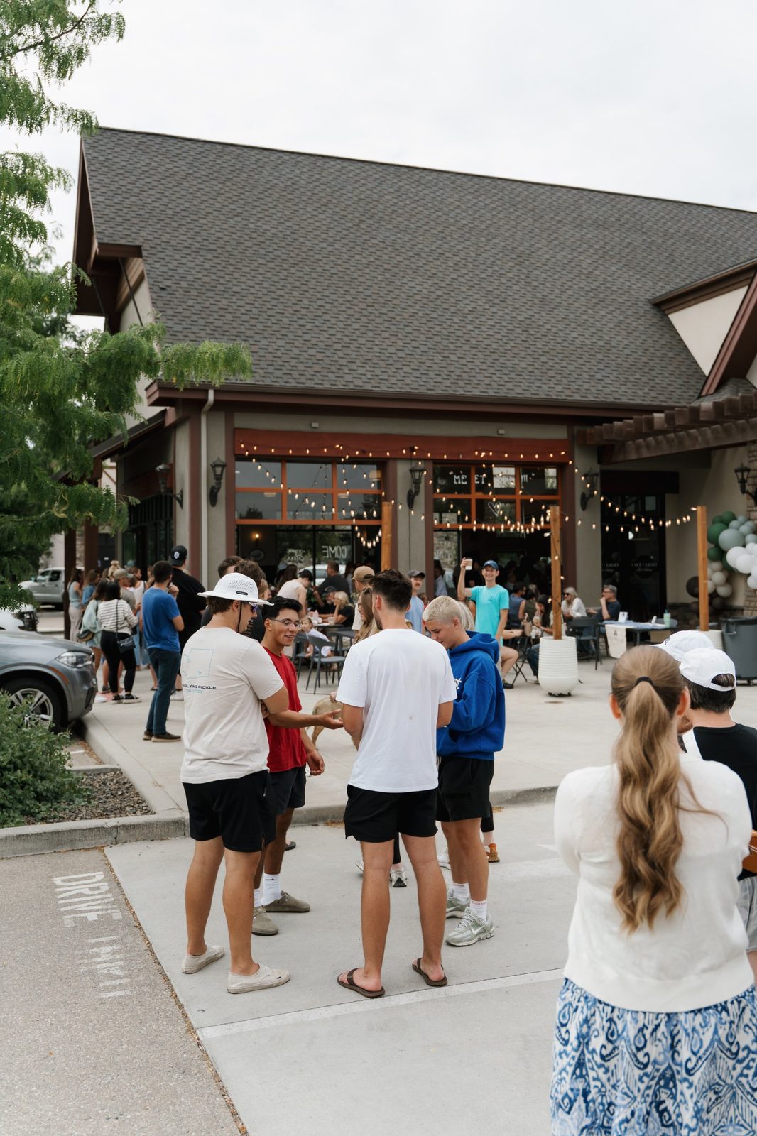 A crowd gathered on the patio and sidewalk outside Salt & Light Coffee Lounge on grand opening day under string lights