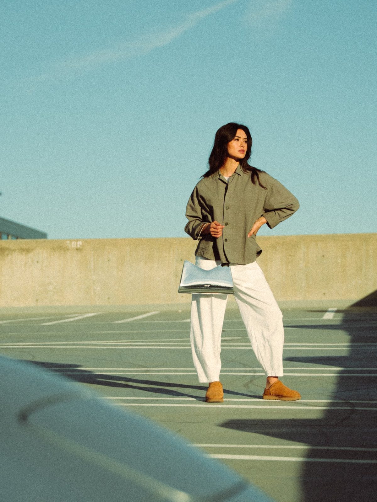 Woman in an olive linen jacket holding a silver handbag on a rooftop parking deck under a clear blue sky, lifestyle photography in Boise, Idaho