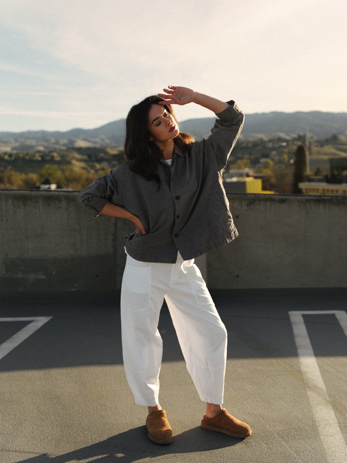 Woman in a gray linen jacket and white wide-leg trousers posing with one arm raised on a Boise rooftop in golden light